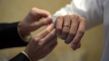 Bir adam diğerinin beyaz gömlek giymesine yardım eder.