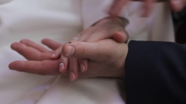 Mani delicatamente collegate di una coppia appena sposata con fedi nuziali su un dito su uno sfondo di un abito da sposa bianco — Video Stock