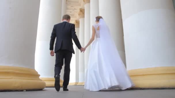 Braut und Bräutigam gehen unter die Säulen — Stockvideo
