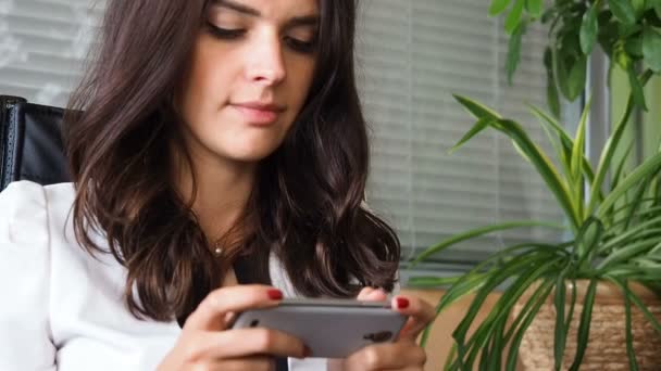 Happy businesswoman playing game on smartphone in office — Stock Video