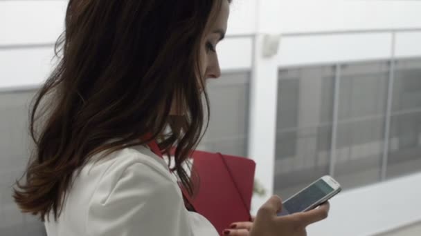 Elegante hermosa mujer mirando en el teléfono inteligente en el edificio de oficinas — Vídeos de Stock