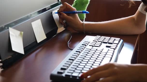 Mujer joven en la oficina escribiendo en pegatina pegada en el monitor — Vídeo de stock