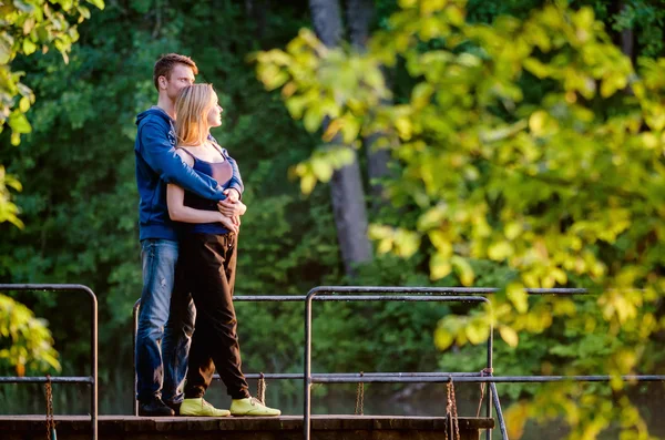 Man hugging his girlfriend at sunset on pier near water Stock Photo