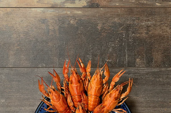 Plate of red crayfishes on old wooden table in bottom part — 图库照片