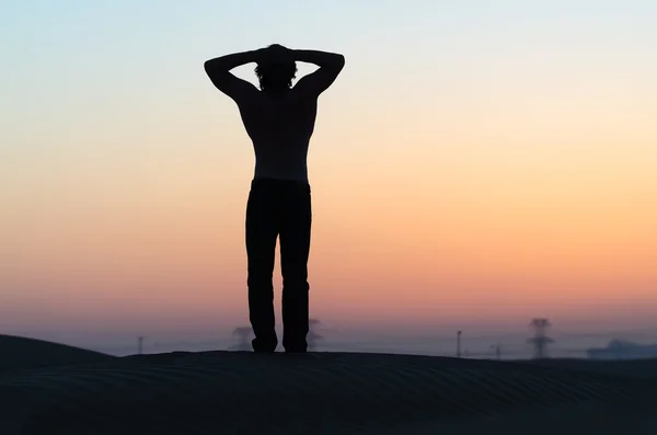 The man silhouette at sunset in desert with hands behind his head