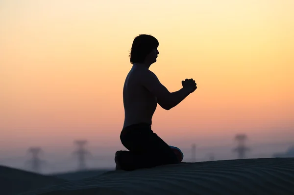 Modlitwa człowieka sylwetka siedzi sama w pustyni na zachodzie słońca — Zdjęcie stockowe