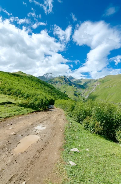 Route avec des traces de pneus menant à des montagnes et de beaux nuages — Photo