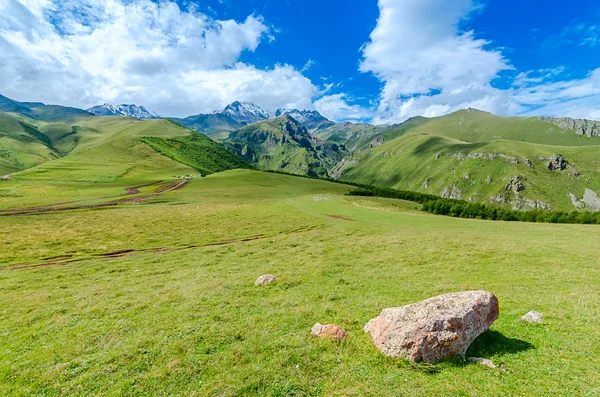 Route avec des traces de pneus menant à des montagnes et de beaux nuages — Photo