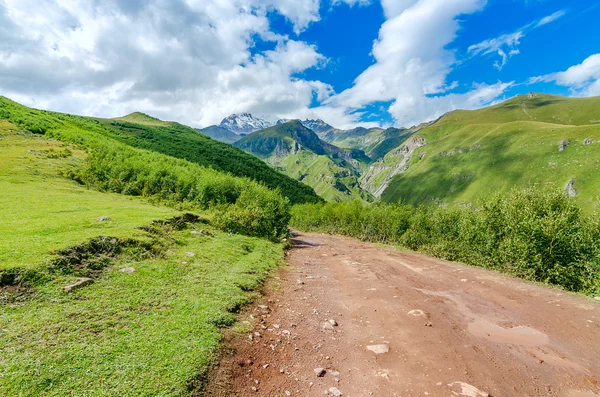 Strada con tracce di pneumatici che portano a montagne e belle nuvole — Foto Stock