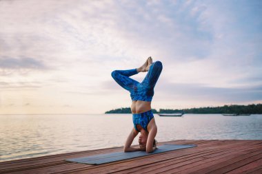 Gün batımı kumsalında yoga yapan genç bir kadın.