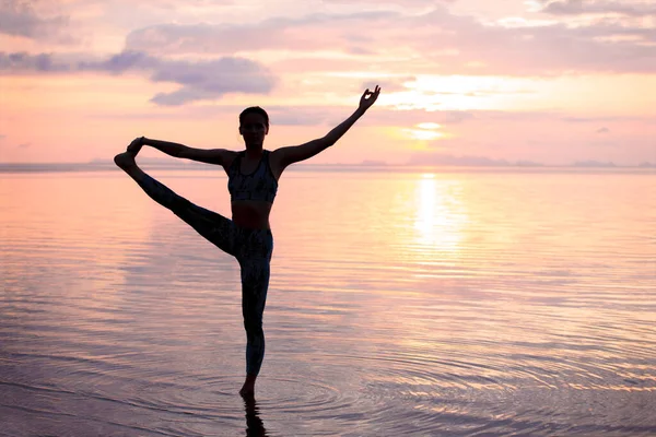 Gün batımı kumsalında yoga yapan siluet kadın.