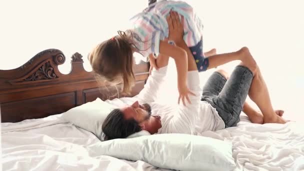 Šťastné rodinné idyly malé dítě dcera skočit na otce zbraně a spadnou na posteli — Stock video