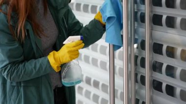 Kadın temizlikçi, koruyucu maske ve eldiven takmış, restoranda ya da kamu kuruluşunda antiseptikle kapı kollarını siliyor. Covid-19 koruması.