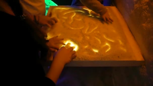 Dívky v solné místnosti si hrají se solí a kreslí vzory na světelný stůl během haloterapie. Detailní záběr rukou — Stock video
