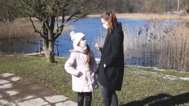 Anne ve kızı kovid 19 koronavirüs enfeksiyonundan korunmak için sağlık maskeleriyle parkta dolaşıyorlar..