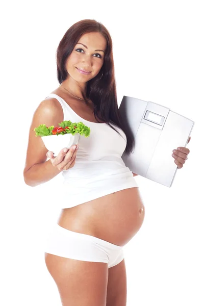Kobieta w ciąży gospodarstwa wagi i jedzenie sałatka. — Zdjęcie stockowe