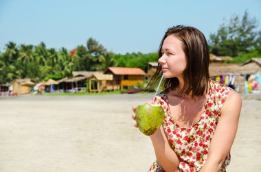 Genç kadın sahilde Hindistan cevizi sütü içme.