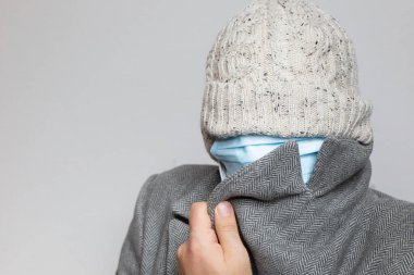 Yüz maskeli ve ceketli bir adam gözleri saklıyor.