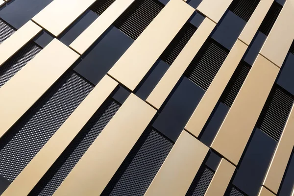 Modern and abstract facade with gold-coloured and black surfaces from an oblique angle, as background to architecture. Horizontal