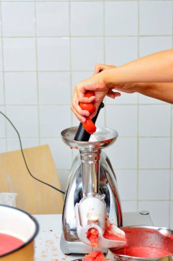 Kız domatesleri meyve sıkacağının içine koyup domates yapıyor..