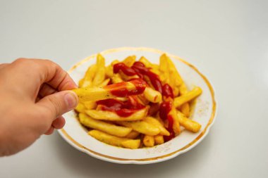 Çocuğun elinde ketçap dökülüp üzerine baharat serpilmiş patates kızartması var..