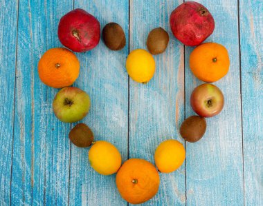 Mavi arka planda çeşitli meyvelerden yapılmış büyük bir kalp yatar..