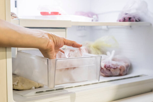 Девушка достает несколько кусочков льда из отсека в морозилку..