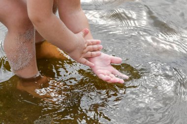 Bir çocuk çamurlu bir gölde ellerini kumdan temizlemeye çalışır..