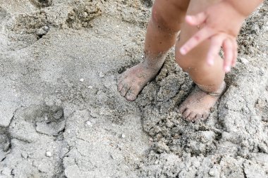 Çocuk ayaklarını çamurlu kumun üzerine sürdü ve şimdi üzerinde duruyor..