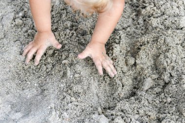 Çocuk bir şey inşa etmek için bir yığın ıslak kum topluyor..
