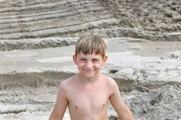A child with a broad smile is standing on the sand, which has many car tire marks.