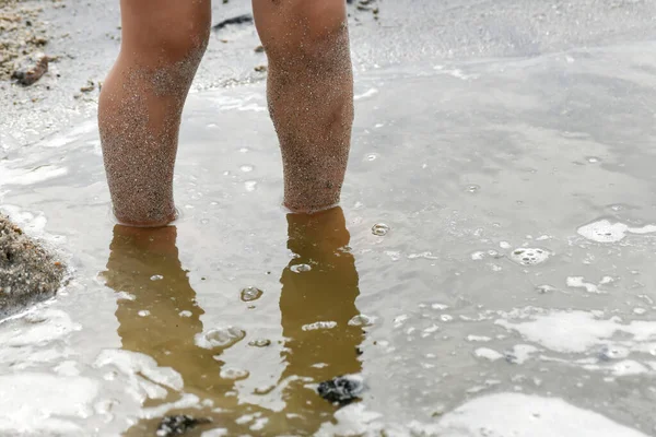 A child with dirty feet stands in a small muddy lake.