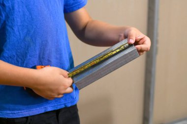 Büyüyen bir işçi bir parça alçı tahtası profilini mezurayla ölçer..
