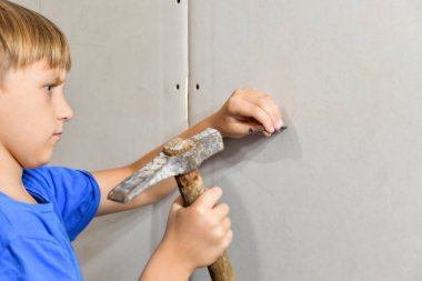 Ciddi yüzlü bir çocuk çekiçle çiviyi alçıpana çakıyor..