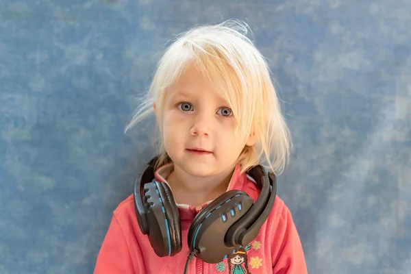 The child has hung the headphones around his neck and looks curiously at the camera.