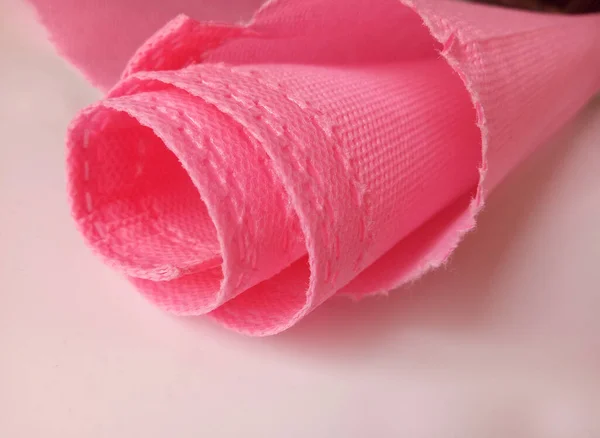 Pembe polipropilen kumaş rulo. Beyaz arka planda pürüzlü kenarları ve gözenekleri olan dokumasız veya polipropilen kumaş