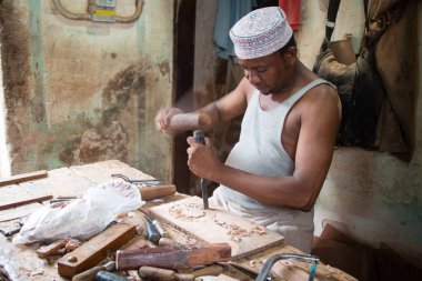 STONETOWN, ZANZIBAR - 1 Ocak 2018: Marangoz, Stonetown, Zanzibar 'da geleneksel el aletleri kullanarak ahşap tahtada süsler yaratıyor