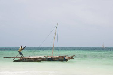 KIWENGWA, ZANZIBAR - 29 Aralık 2017: Kiwengwa plajı yakınlarındaki geleneksel ahşap dwhow teknesini iten yerel adam, Zanzibar