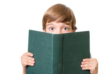 Genç sevimli çocuk beyaz arka planda izole edilmiş büyük bir kitabın arkasından şaşırmış görünüyor.