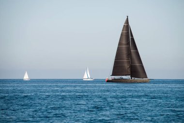 Black and two white sailing yachts on the sea with clear blue sky