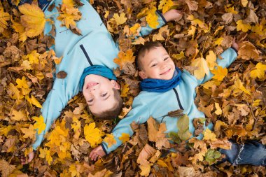 Sonbahar parkında düşen yaprakların üzerinde yatan kardeşler. 