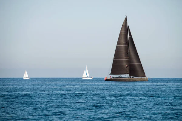Black and two white sailing yachts on the sea with clear blue sky
