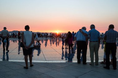 ZADAR, CROATIA - SEPTEMBER 1, 2016: Siluetli insanlar Hırvatistan 'ın Zadar kentindeki mimar Nicola Basiç' in Güneş 'e Selamlar adlı yuvarlak güneş paneli kentsel kurulumunda Adriyatik üzerinde gün batımını izliyorlar