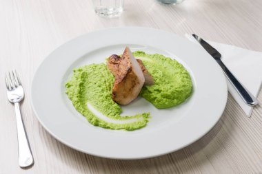 Tabakta yeşil bezelye püresiyle ızgara tavuk bifteği.