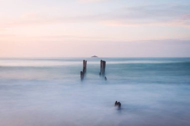 Şafak vakti Dunedin 'deki St. Clair Plajı' nda eski iskele yığınları.