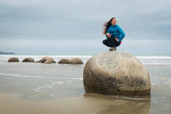 Yeni Zelanda 'nın doğu kıyısındaki Koekohe sahilinde Moeraki Boulder' ın tepesinde poz veren genç bir kadın.