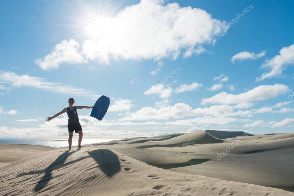 young woman posing with board at Te Paki sand dunes, New Zealand