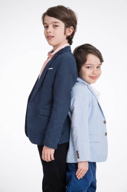 Beyaz arka planda sırt sırta duran takım elbiseli iki genç çocuk.