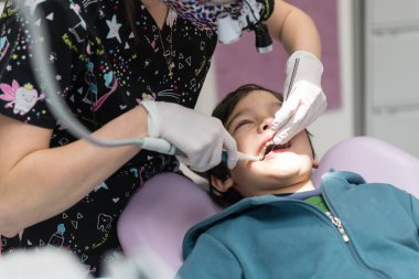 Klinikte genç çocuğun dişlerini muayene eden dişçi.