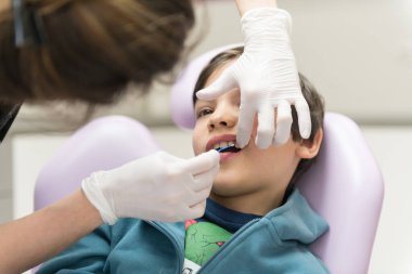 Dişçi klinikte küçük çocuğun dişlerini muayene ediyor.